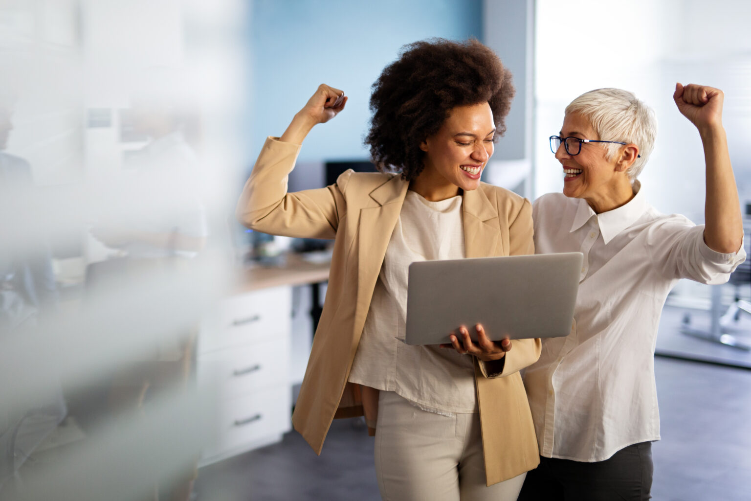 Happy multiethnic business women working together online on a laptop in corporate office.